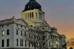 The state capitol building with a sunrise in the background.