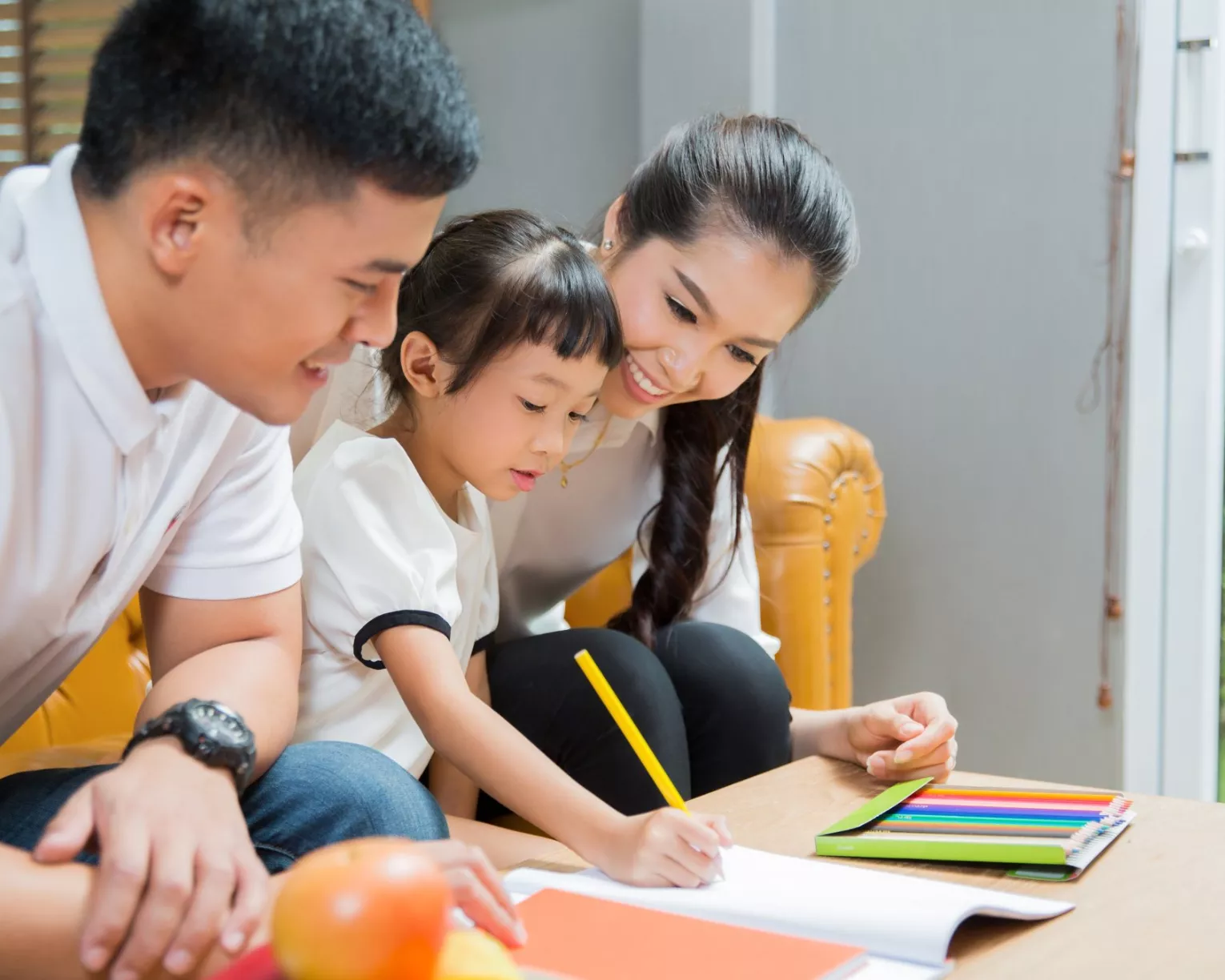 A family sits with a small child looking over their homework.