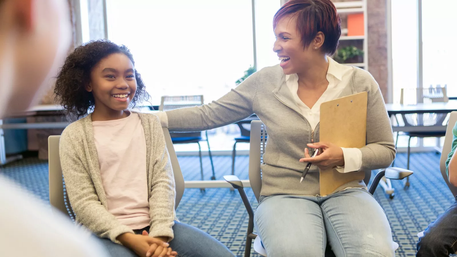 An educator smiles at a student and pats them on the back in a classroom circle.