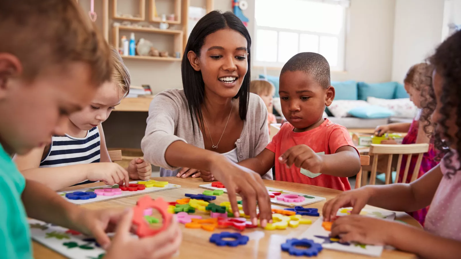A teacher sits with kindergartners helping as they work with manipulatives