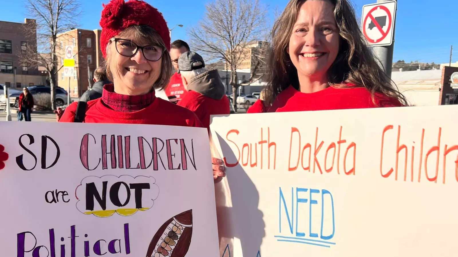 two smiling members hold signs that say "SD children are not political footballs" and "South Dakota children NEED age-appropriate learning." - 3840x2160