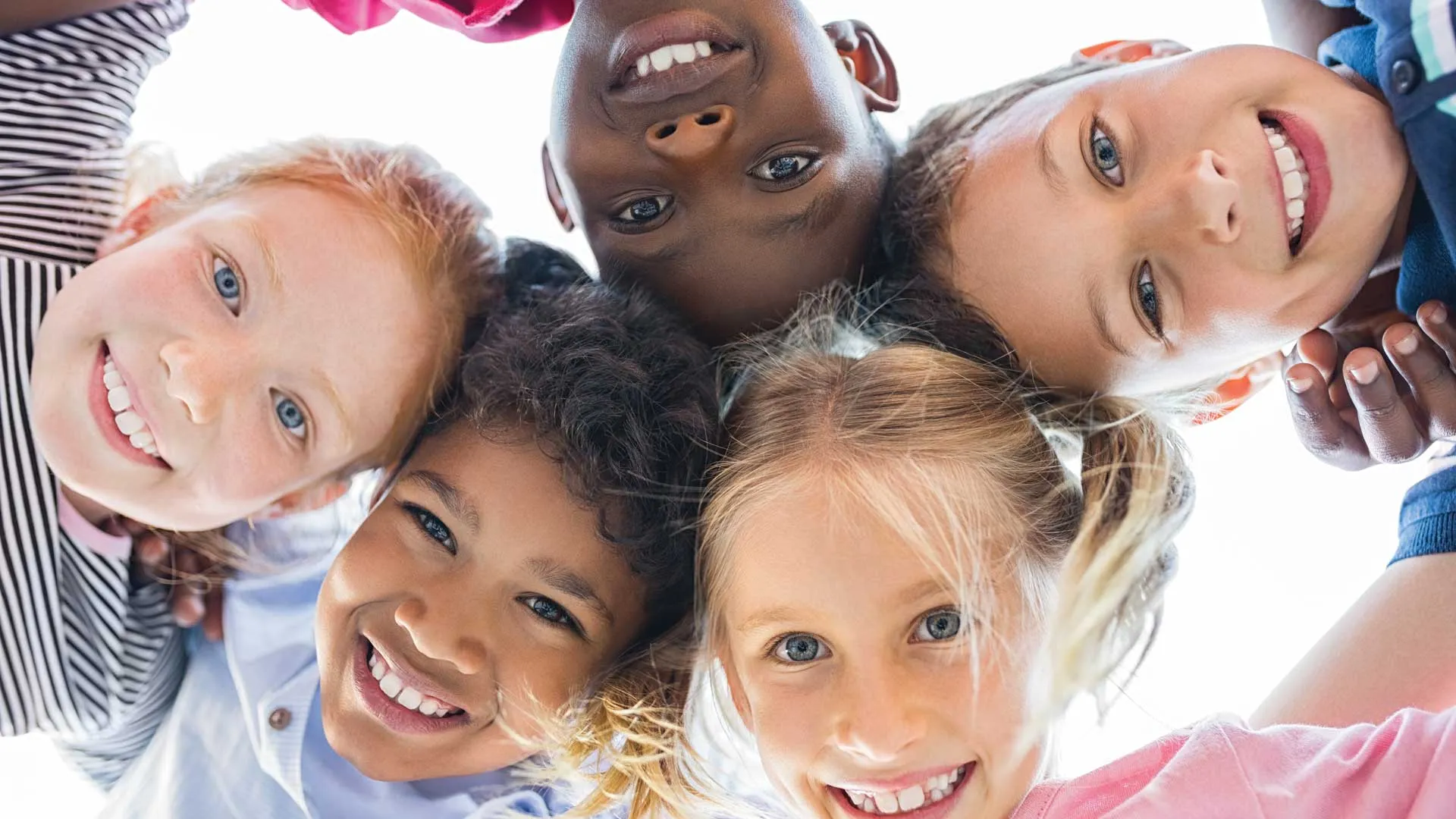 Diverse group of children with their heads touching looking down.