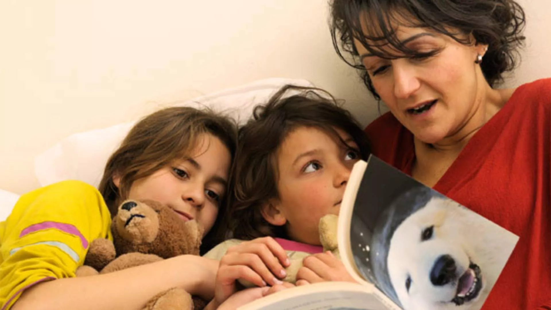 A mom reads a book with her children in bed