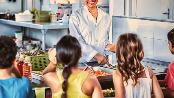A smiling lunch lady serves delicious looking healthy food to elementary school students.