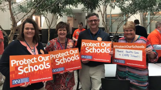 SDEA members pose for a photo at NEA headquarters with signs that say "Protect Our Schools."