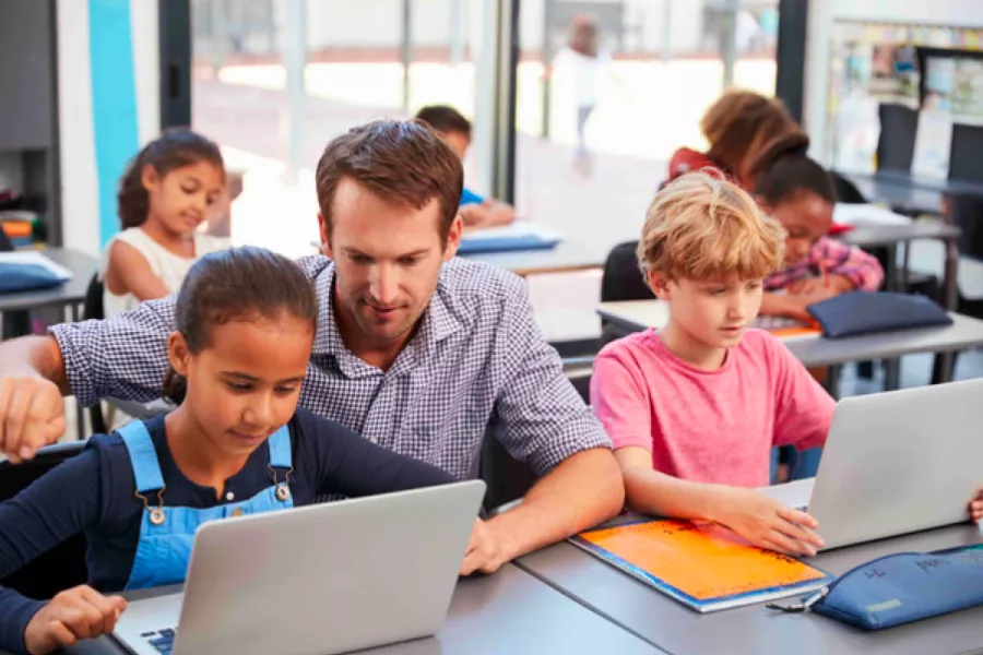 A teacher helps students working on laptops
