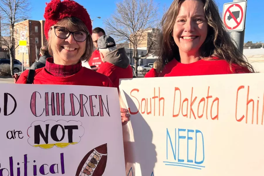 two smiling members hold signs that say "SD children are not political footballs" and "South Dakota children NEED age-appropriate learning." - 3840x2160